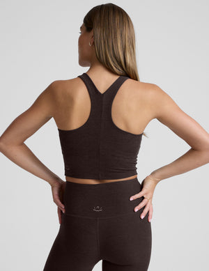 woman wearing a brown high neck racerback cropped tank and leggings on a plain background. 