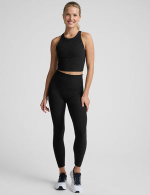 woman wearing a black high neck racerback cropped tank on a plain background. 