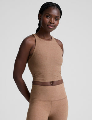 woman wearing a brown high neck racerback cropped tank top and leggings on a plain background. 