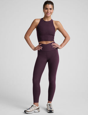 model wearing a purple high neck racerback cropped tank top and purple high-waisted midi length leggings against a plain background. 