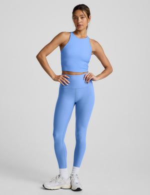 Woman wearing a blue high neck racerback cropped tank on a light gray background. 