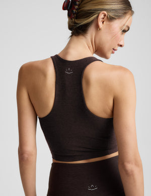 Woman wearing a brown v-neck racerback cropped tank and leggings on a light gray background. 