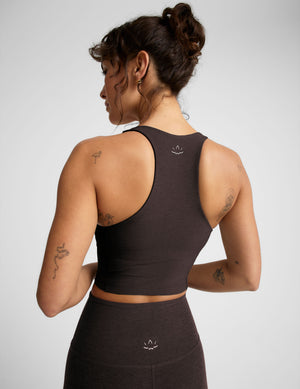Woman in brown v-neck cropped racerback tank and brown leggings against a plain background. 
