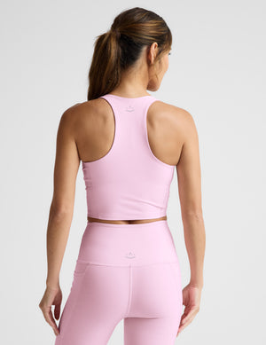 Woman wearing a pink cropped tank and leggings on a light gray background. 