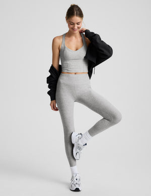 Woman wearing a grey v-neck racerback cropped tank and leggings against a plain background. 
