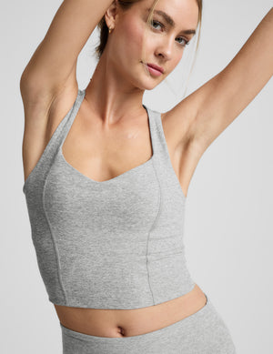 Woman wearing a grey v-neck racerback cropped tank and leggings against a plain background. 