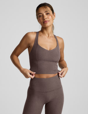 Woman wearing a brown v-neck racerback cropped tank and leggings on a light gray background. 