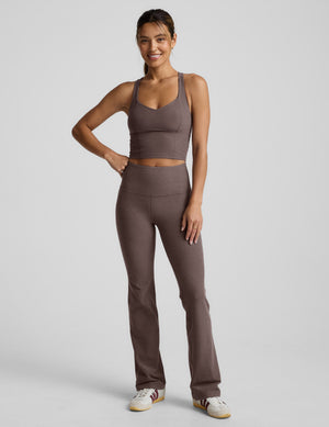 Woman wearing a brown v-neck racerback cropped tank and leggings on a light gray background. 