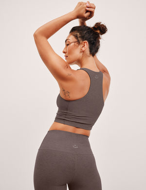 Woman in brown v-neck cropped racerback tank and leggings against a grey background. 