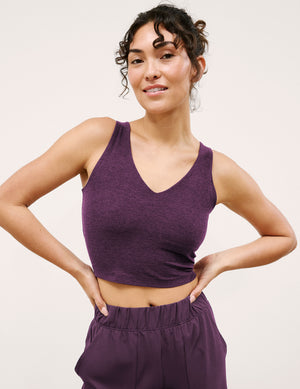 Woman wearing a purple tank top and pants against a plain background. 