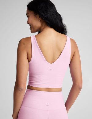 Woman wearing a pink v-neck cropped tank and leggings against a plain background. 