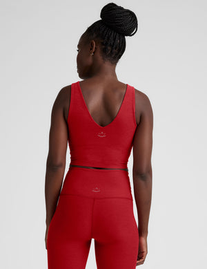 woman wearing a red v-neck cropped tank and leggings on a plain background. 
