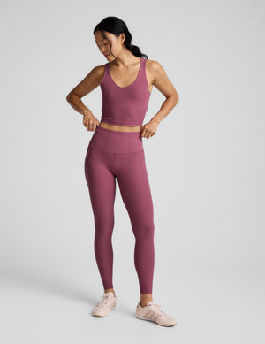 Woman wearing a v-neck cropped tank and leggings against a plain background. 