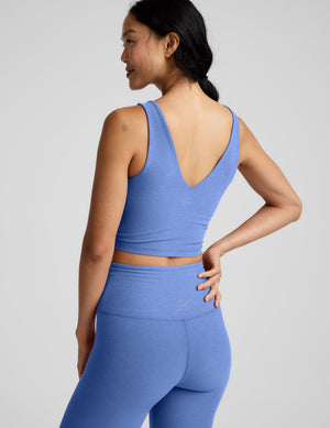 Woman wearing a blue cropped v-neck tank and leggings against a plain background. 