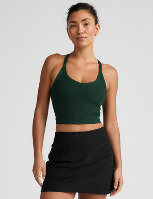 model wearing a green v-neck cropped tank top with a high racerback and black mini athletic skirt against a plain background. 