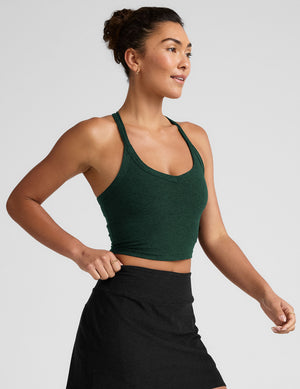 model wearing a green v-neck cropped tank top with a high racerback and black mini athletic skirt against a plain background. 