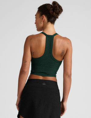 model wearing a green v-neck cropped tank top with a high racerback and black mini athletic skirt against a plain background. 