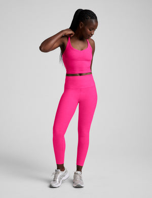 Woman wearing a pink v-neck cropped tank and leggings against a plain background. 