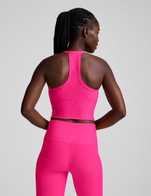 Woman wearing a pink v-neck cropped tank and leggings against a plain background. 