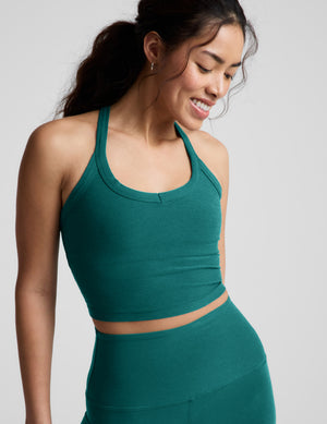Woman wearing a green cropped tank top and leggings against a plain background. 