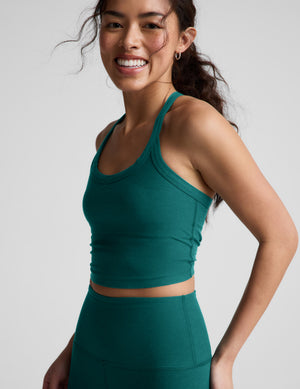 Woman wearing a green cropped tank top and leggings against a plain background. 