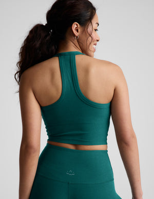 Woman wearing a green cropped tank top and leggings against a plain background. 