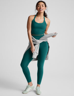 Woman wearing a green cropped tank top and leggings against a plain background. 