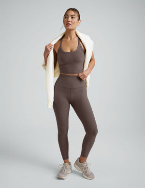 Woman wearing a brown v-neck high racerback cropped tank and leggings on a light gray background. 