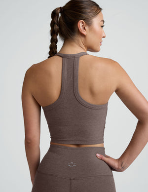 Woman wearing a brown v-neck high racerback cropped tank and leggings on a light gray background. 
