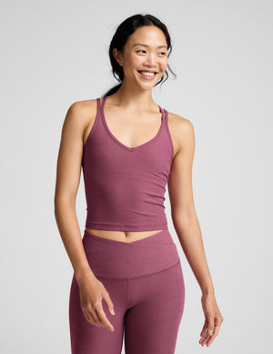 Woman wearing a purple v-neck tank top with crossover back straps and leggings against a plain background. 
