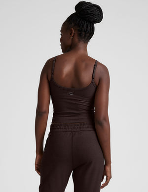Woman wearing a brown midway length tank top with adjustable straps and brown jogger pants against a plain background. 