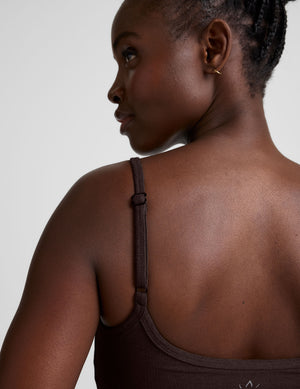 Woman wearing a brown midway length tank top with adjustable straps against a plain background. 