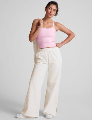 Woman wearing a pink tank top and white fleece pants against a plain background. 