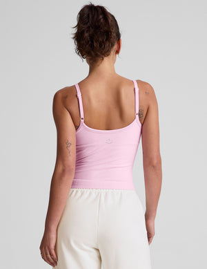 Woman wearing a pink tank top and white fleece pants against a plain background. 