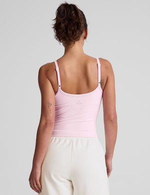 Person wearing a light pink tank top and white pants on a plain background