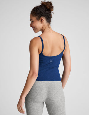 Woman wearing a blue tank top and gray leggings against a light gray background. 