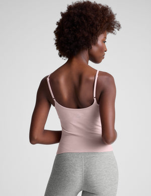 Woman wearing a light pink tank top and gray leggings against a plain background. 