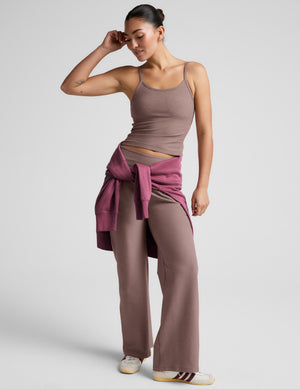 Woman wearing a brown tank top and pants against a plain background. 