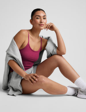 Woman wearing a red tank top and grey sweat shorts against a plain background. 