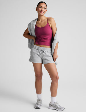 Woman wearing a red tank top and grey sweat shorts against a plain background. 