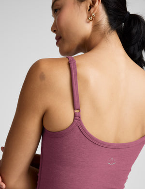 Woman wearing a purple waist length tank and leggings against a plain background. 