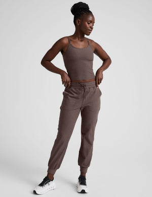 Woman wearing a brown mid length tank top and joggers against a plain background. 
