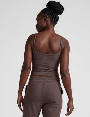 Woman wearing a brown mid length tank top and joggers against a plain background. 