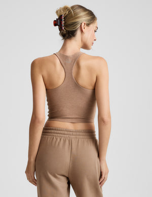 Woman wearing a brown high-neck racerback cropped tank and brown fleece pants against a plain background. 