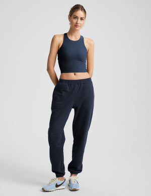 Woman wearing a blue high-neck cropped racerback tank and blue joggers against a plain background. 
