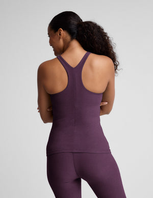 Woman wearing a purple sleeveless top and leggings on a plain background. 