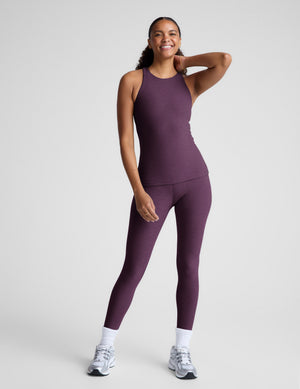 Woman wearing a purple sleeveless top and leggings on a plain background. 