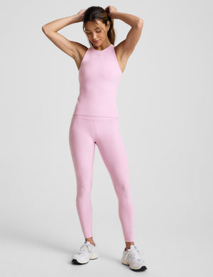 Woman wearing a pink racerback sleeveless top and leggings on a light gray background. 