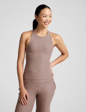 Woman wearing a brown high-neck tank top and pants against a plain background. 