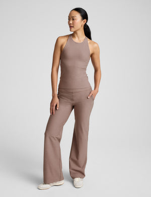 Woman wearing a brown high-neck tank top and pants against a plain background. 